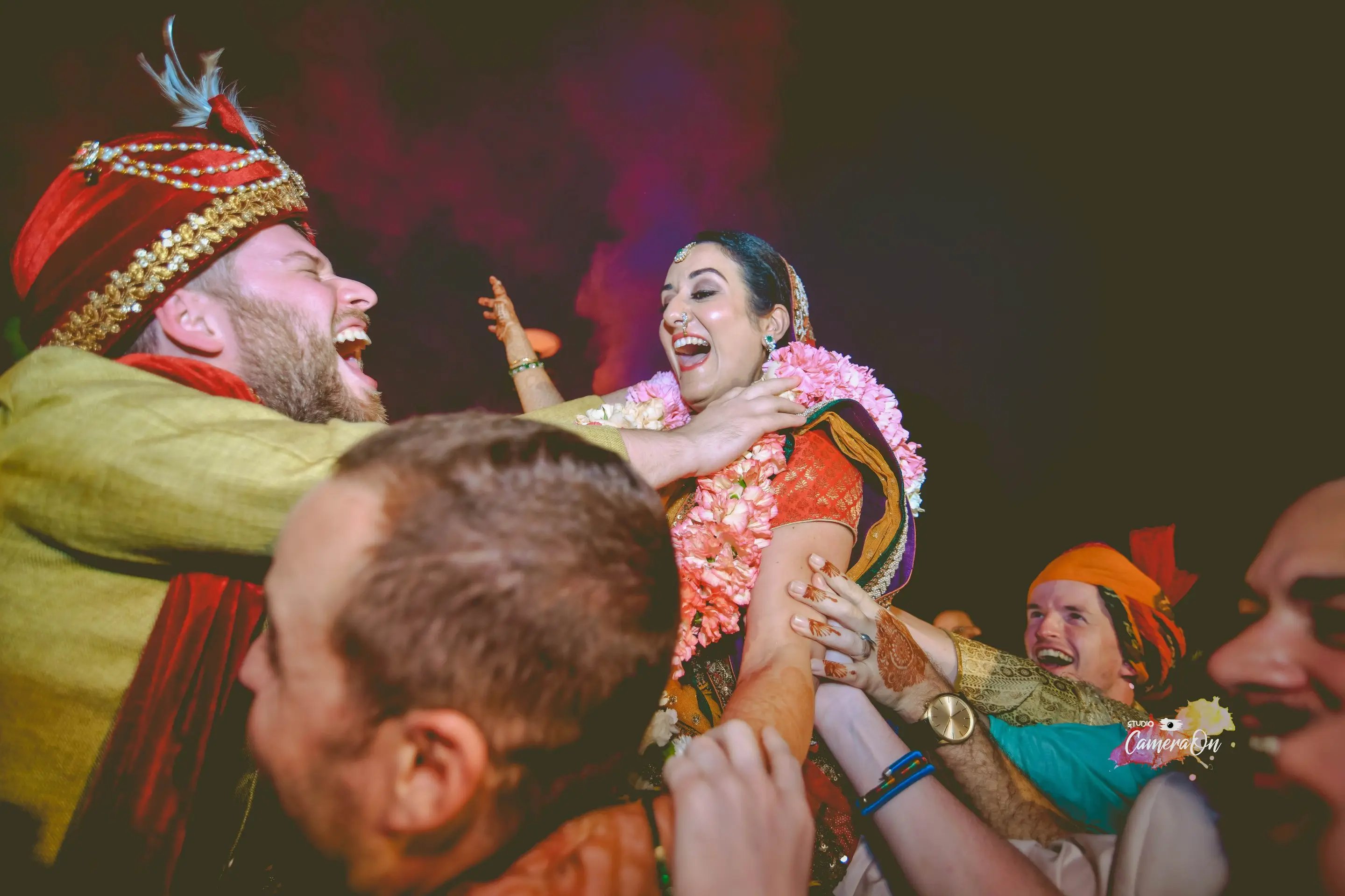 Groom lifted by friends as the bride celebrates at a colourful baraat