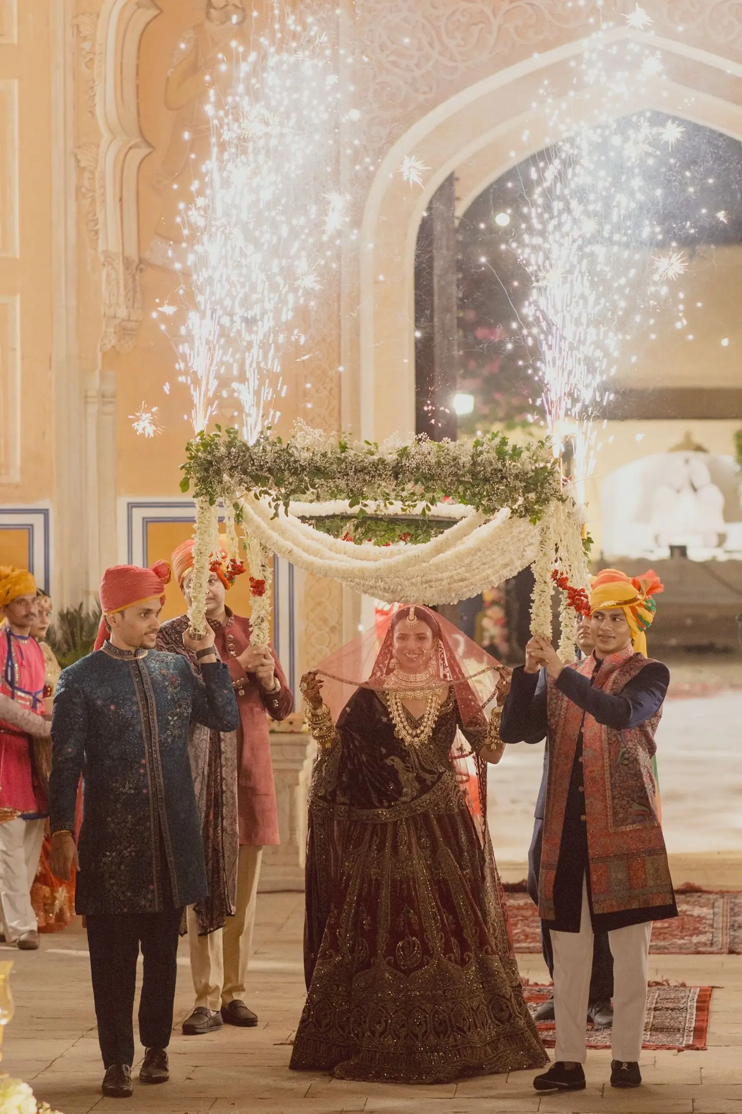 Bride entering under a floral phoolon ki chadar with cold sparklers behind