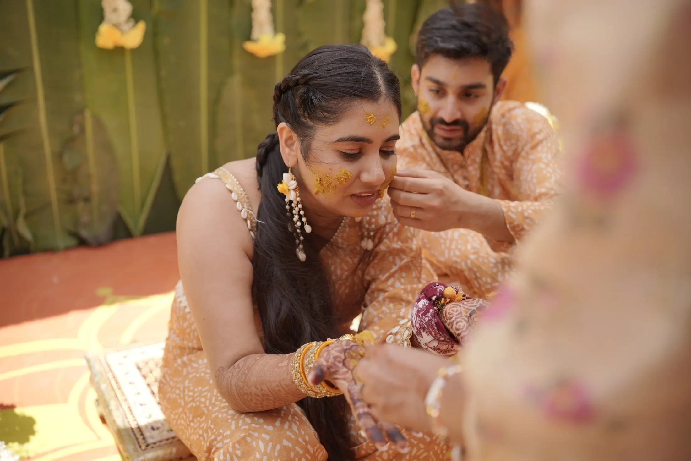 Bride and groom applying haldi together surrounded by family