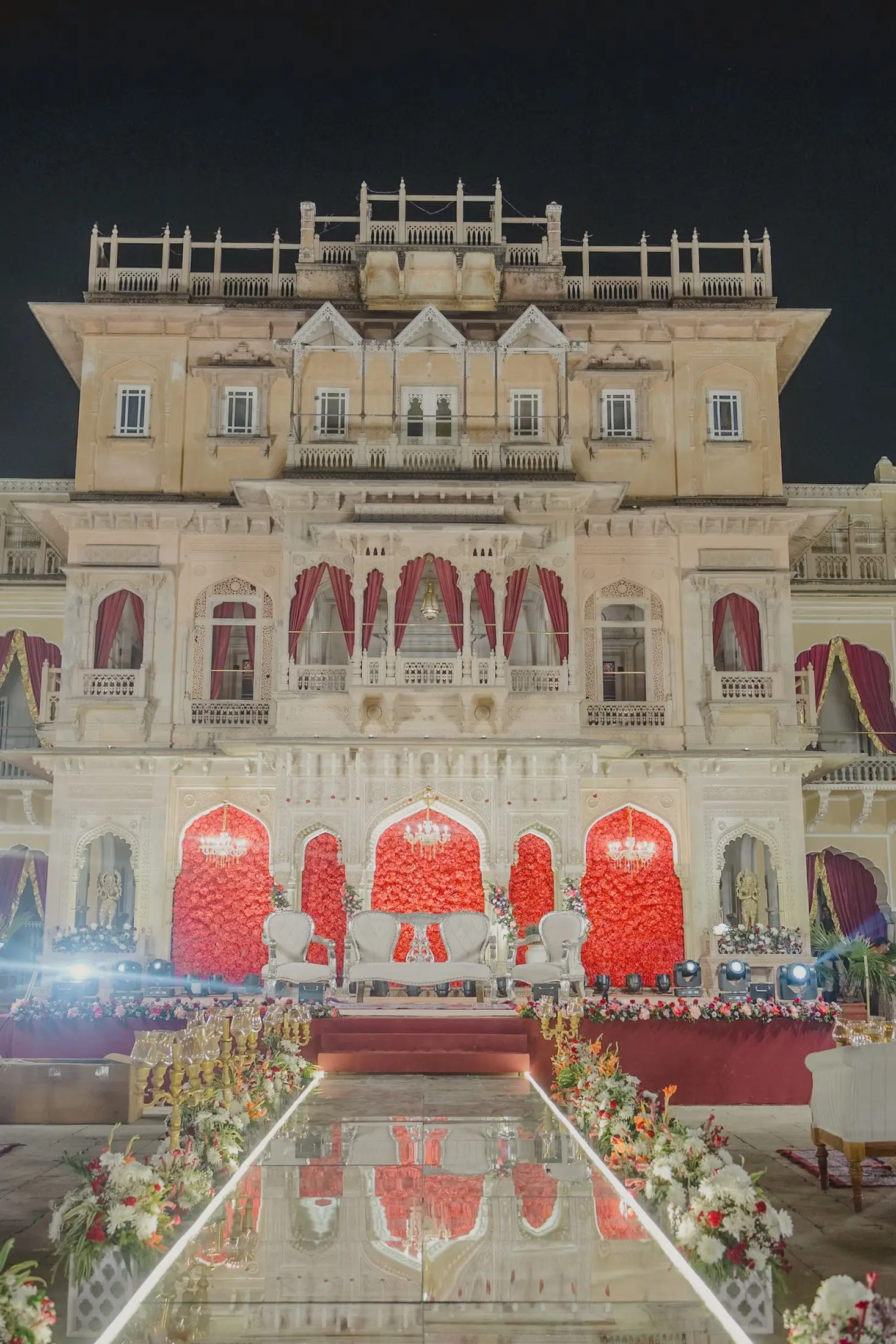 Palace facade lit at night with a reflective aisle lined with flowers